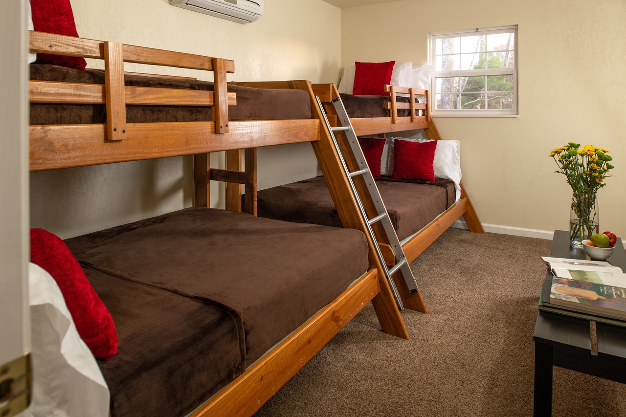 Double wooden bunk bed with ladder in between leading to top bunks, coffee table with fresh flowers in glass vase