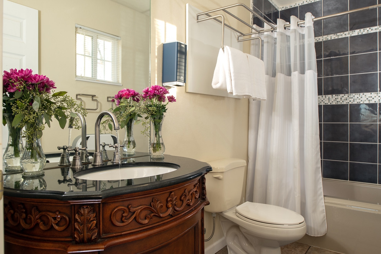 Bathroom with ornately carved wooden vanity with sink, toilet, and tiled shower