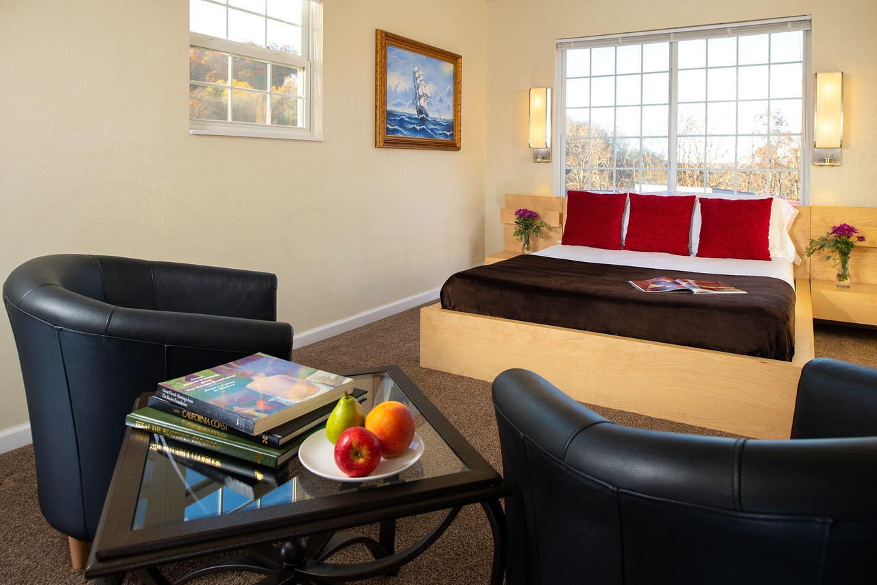 Master bedroom with sitting area with two black leather barrel chairs and end table in foreground and bed in background