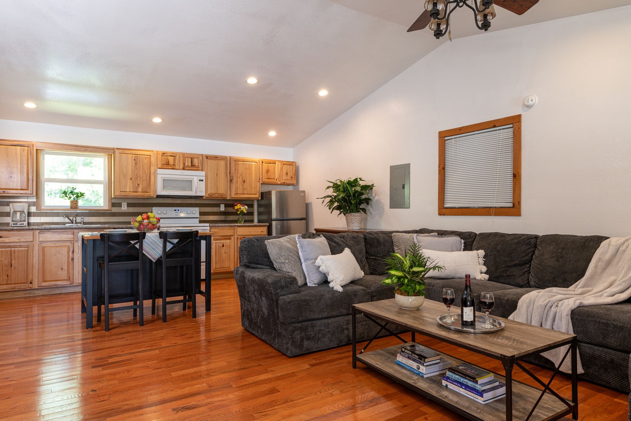 Comfy black sectional couch, hardwood floors, and well-equipped kitchen in background