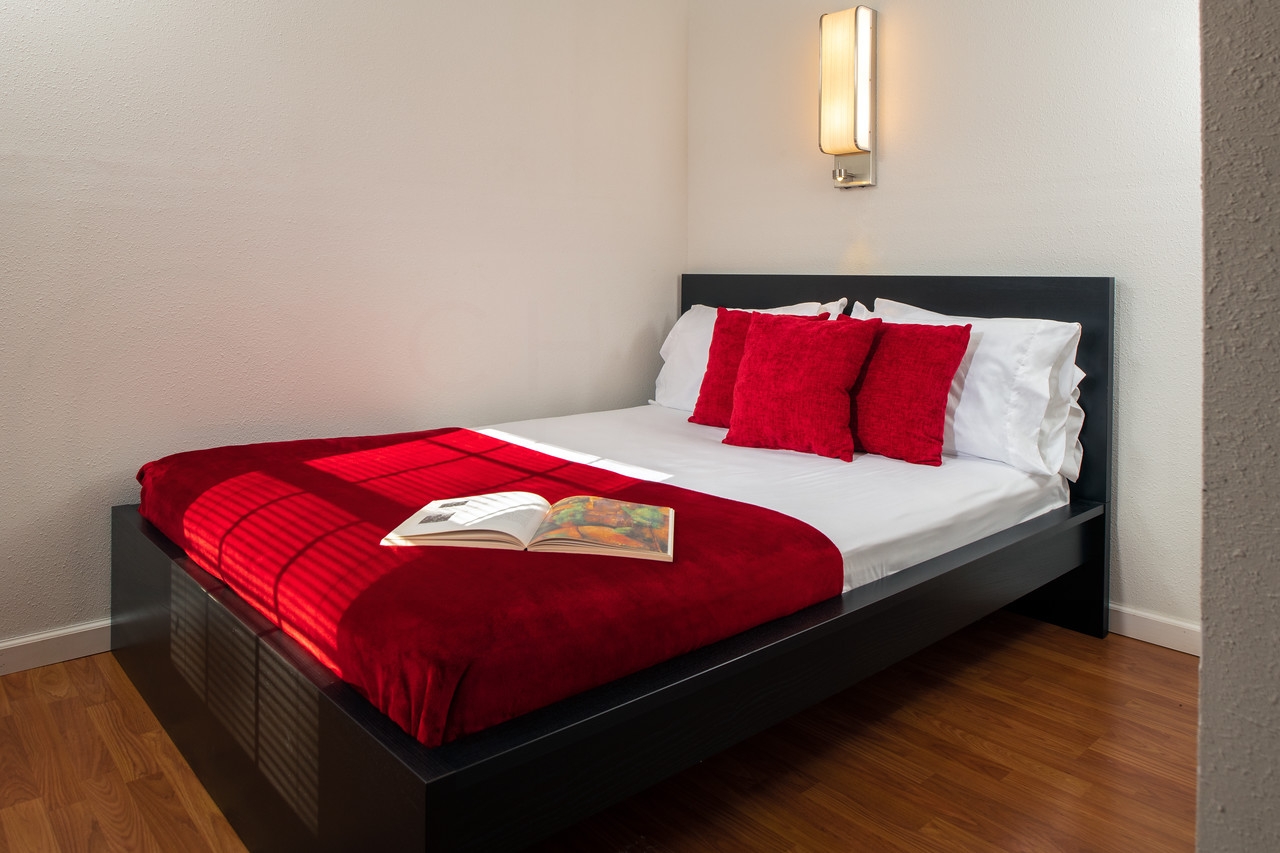 Second bedroom with black wooden platform bed, white sheets, red blanket & red throw pillows