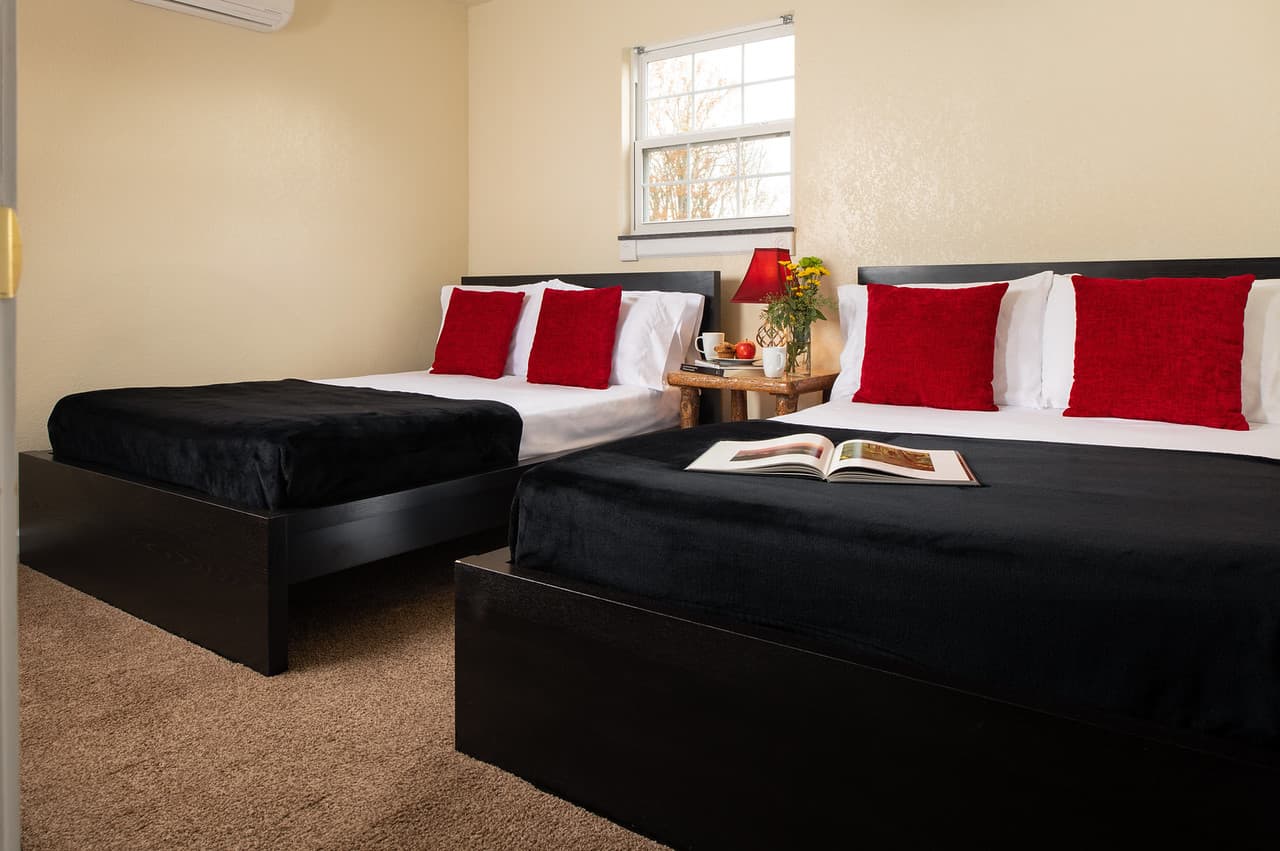 Bedroom with two double beds made with black covers, white sheets, and red throw pillows