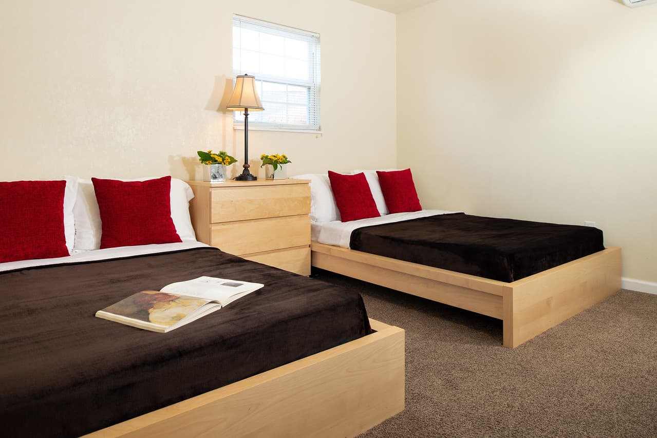 Two queen beds in a room with chest of drawers with table lamp