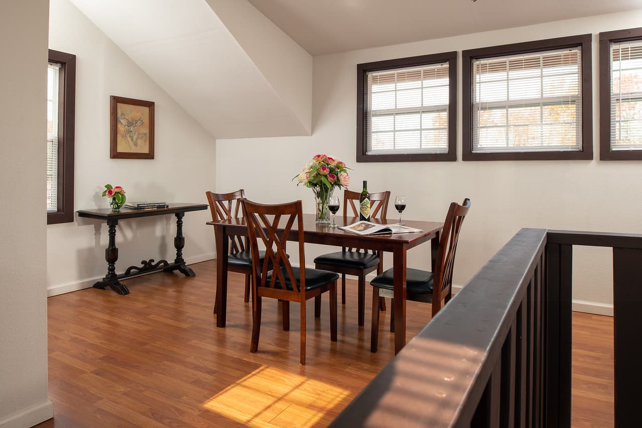 Upstairs dining area with table and chairs for four, matching side table, sunny windows, and hardwood floor