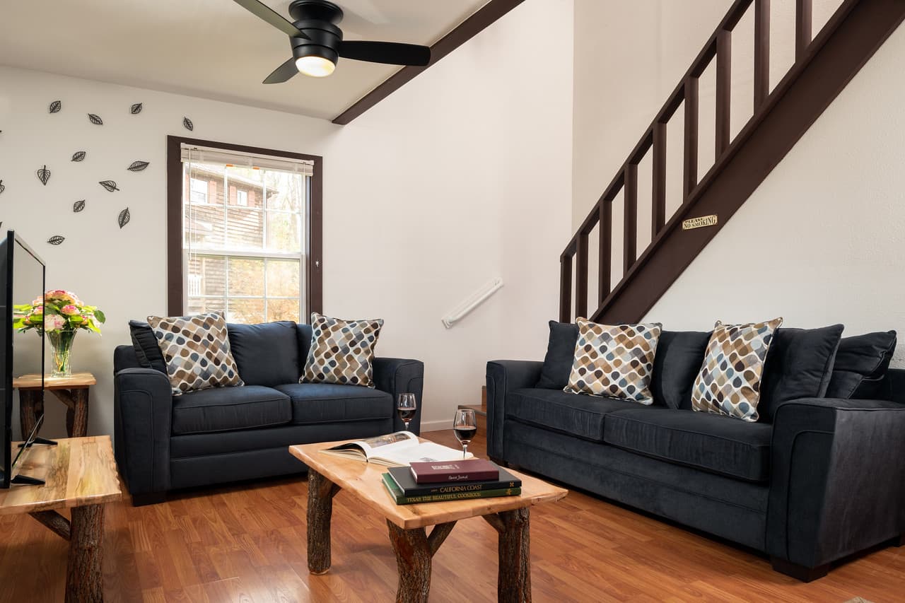 Front sitting room with loveseat and sofa, log coffee table, and TV stand with flat-screen TV, ceiling fan, and staircase to second floor