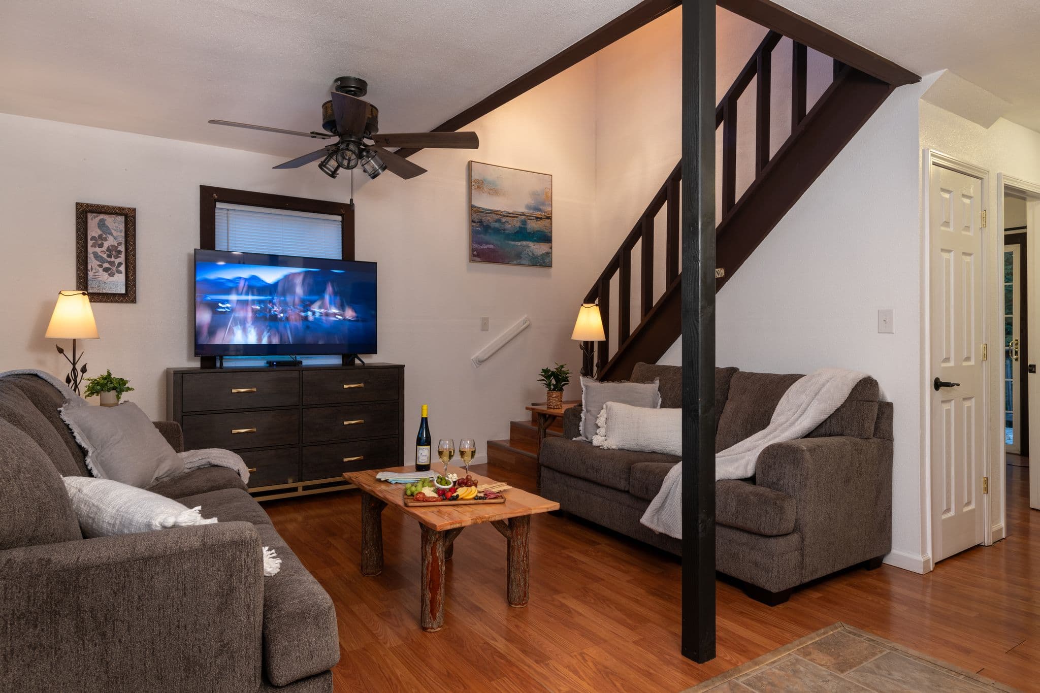 Front sitting room with loveseat and sofa, log coffee table, and TV stand with flat-screen TV, ceiling fan, and staircase to second floor