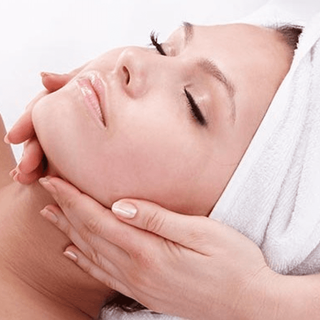 Woman laying on her back with hair in towel and masseuse massaging neck