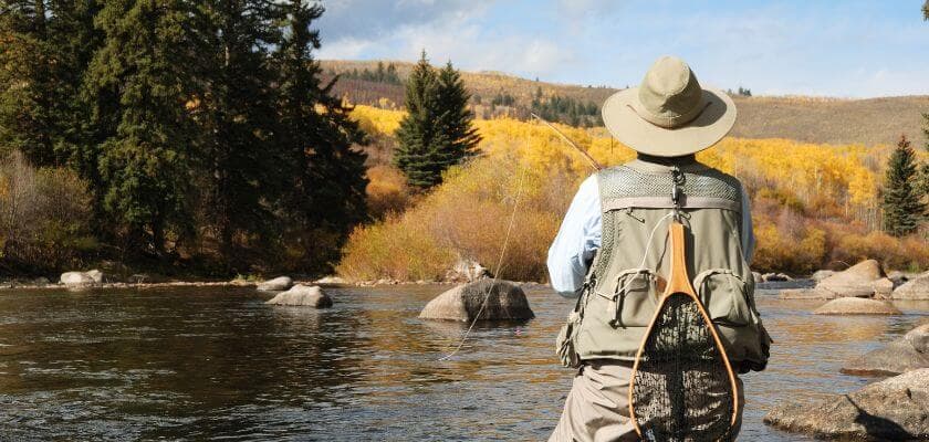 A person fishing in a river surrounded by autumn foliage and rocky banks.