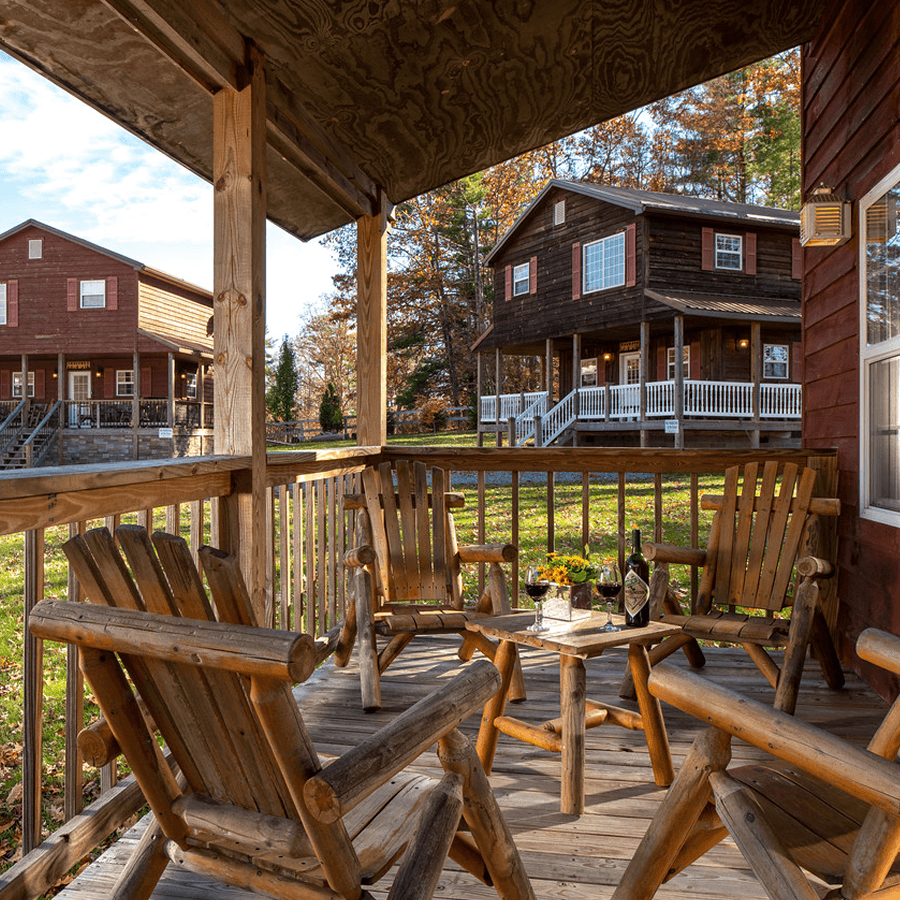 front porch of chalet, heavy wood furniture, chairs, low table, with drinks in glasses and other chalets in the background