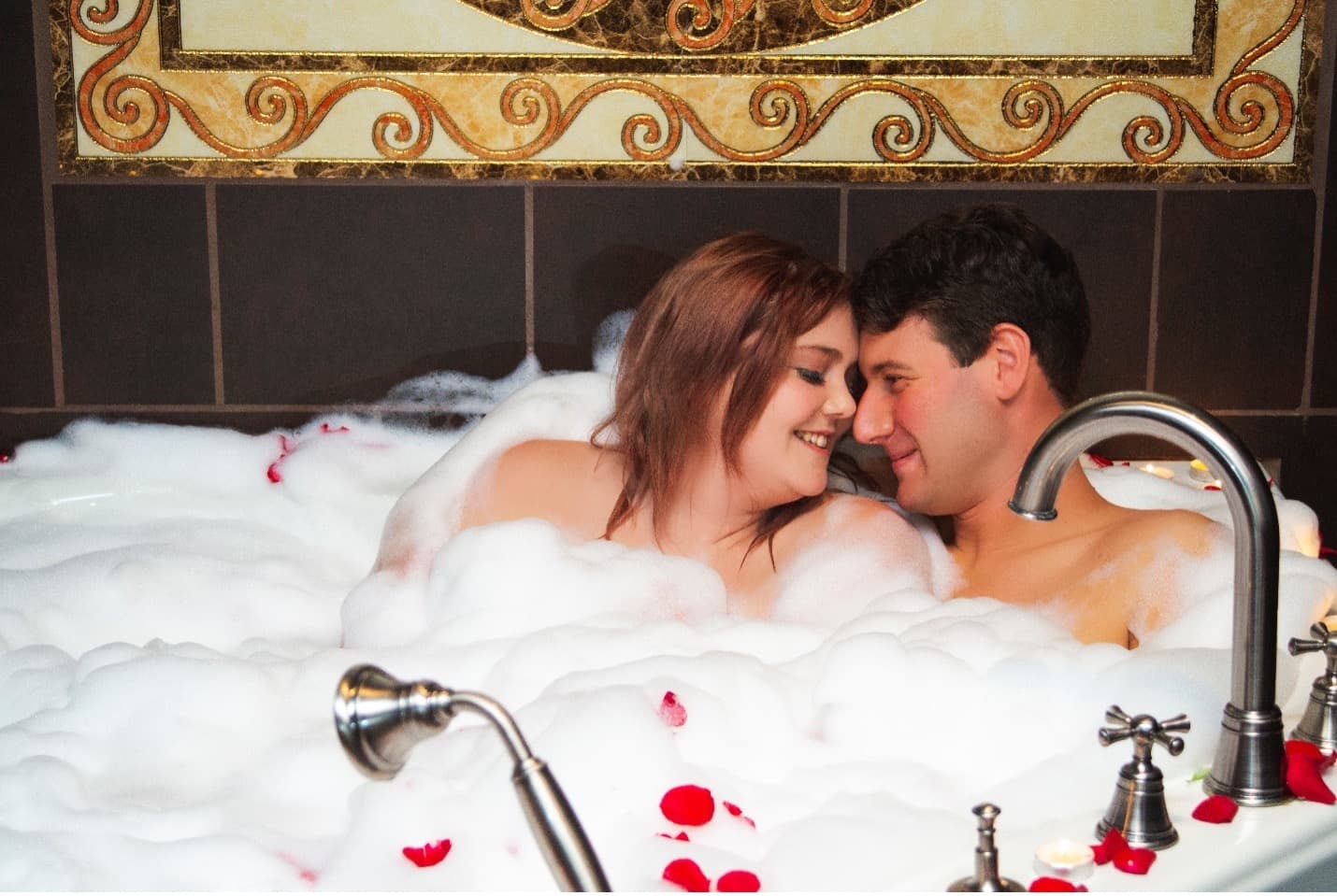 Man and woman in corner bath tub with bubble and red rose petals