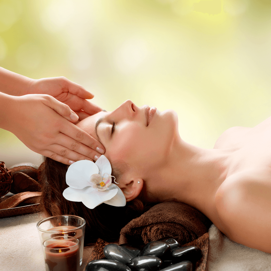 Woman laying on back with flower over her ear, with a masseuse hands massaging her temples