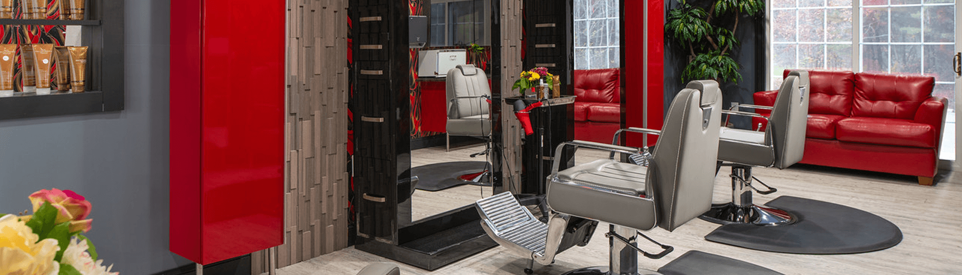 Red and black decor, red leather couch, grey salon chair in middle of room in front of mirrored wall.