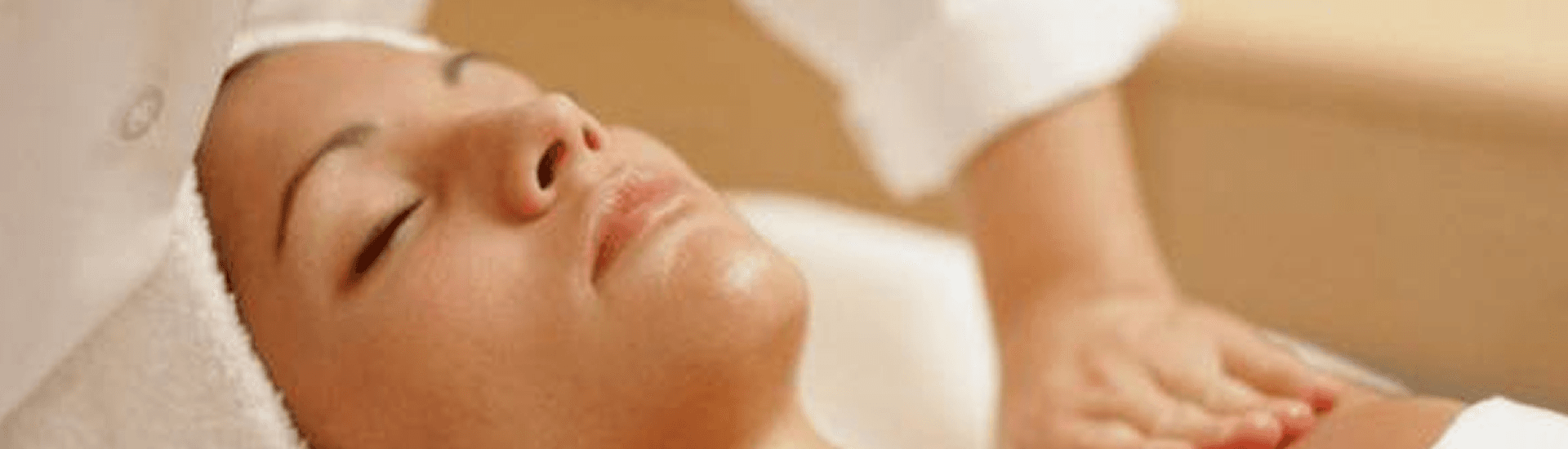 Woman on her back in a towel with her eyes closed being massaged