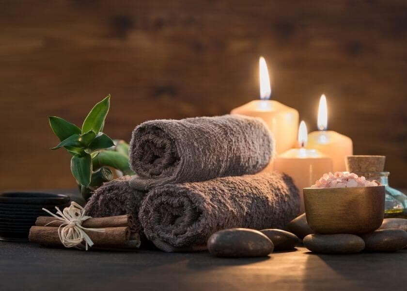 Two rolled towels beside candles, stones, and a bowl of salt, set in a tranquil spa environment. Two rolled towels beside candles, stones, and a bowl of salt, set in a tranquil spa environment.